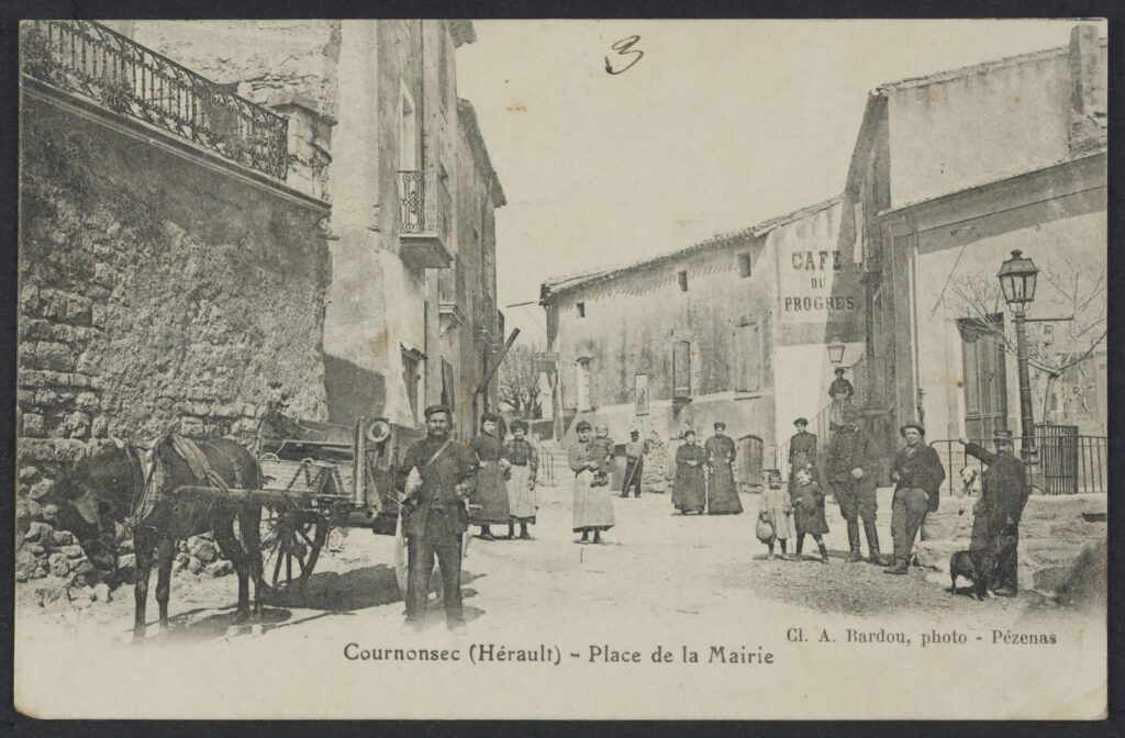 Vielle photo sépia d'une scène de vie sur la Place de la Mairie de Cournonsec. Cheval tirant une calèche dans rue animé près du café du Progrès